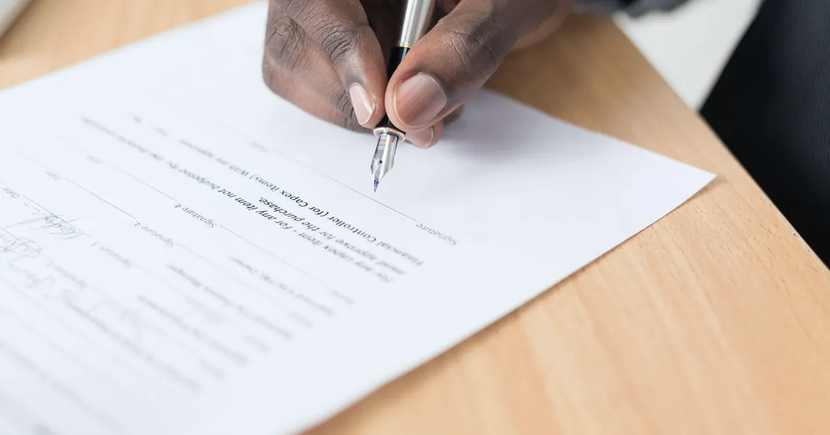 Hand signing an insurance document on a wooden desk
